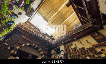 A view looking up at a beautifully designed courtyard with wooden shutters and greenery. The open sky is visible through the slats, creating a serene Stock Photo