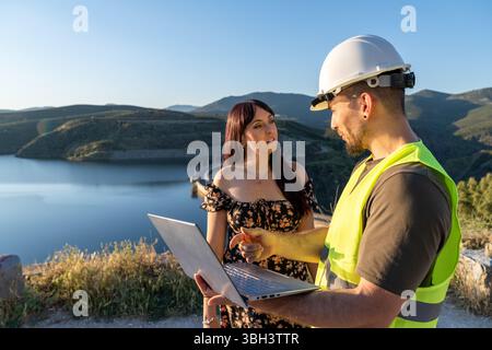 Engineers discussing a project using a laptop near a dam Stock Photo