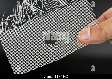 A hand holds damaged wire mesh with hole, possibly caused by rat. mesh is frayed and shows signs of wear, highlighting need for repair or replacement Stock Photo