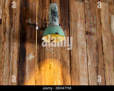 A weathered, vintage style hanging lamp mounted on a natural wooden plank wall Stock Photo