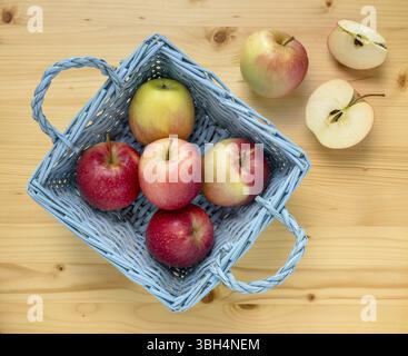 Red apples in blue wooden basket on wooden table. Two apples are remained out of the basket and one is cut. Top view Stock Photo