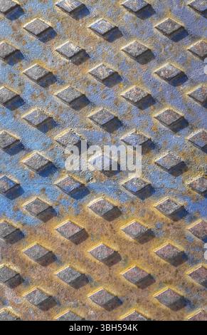 Old rusty drain cover background with diamond pattern. Orange and blue rusted manhole texture with square pattern, background macro Stock Photo
