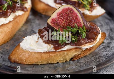 Canape or crostini with toasted baguette, cream cheese, onion jam, figs and fresh thyme on a tin tray. Ideal appetizer as an aperitif Stock Photo