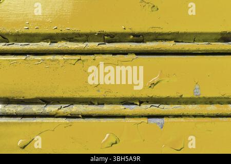 Background of old metal sheet with peel paint texture surface. Painted metal roller shutters door with peeling paint dirty yellow hue. Grungy backgrou Stock Photo
