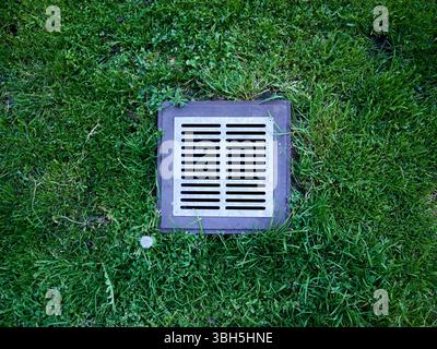 Drain grate is in the grass. The grate is silver and has a black border Stock Photo
