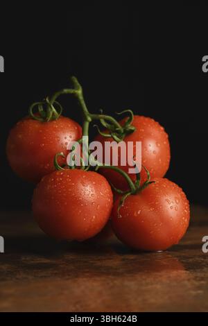 Fresh ripe red tomato branch on a rusty, redhead table with water drops. Dark background. Close-up. Vertical photo. Poster for vegetable market or sho Stock Photo