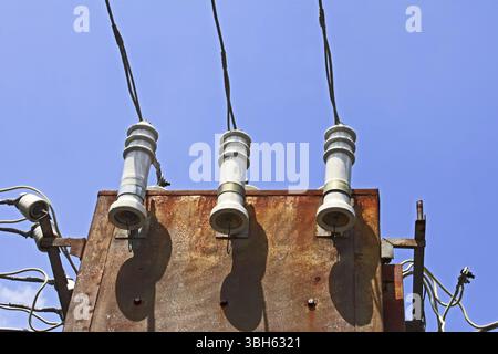 Electric insulators and wires on the old three-phase electrical transformer on a background of blue sky Stock Photo