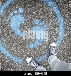 Man standing on blue dot. Sign painted on the pavement reminding users to maintain a physical distance of 3 feet / 1 meter during the COVID-19 pandemi Stock Photo
