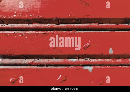 Background of old metal sheet with peel paint texture surface. Painted metal roller shutters door with peeling paint dirty red hue. Grungy background Stock Photo