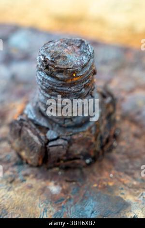 Rusty bolt sits on a piece of metal. The bolt is surrounded by a lot of rust and has a worn appearance. Concept of decay and abandonment, as the bolt Stock Photo