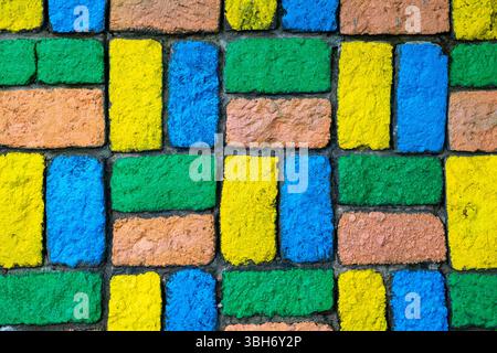 Colorful brick wall with a yellow brick in the middle. The wall is made of different colored bricks, including blue, green, and yellow Stock Photo