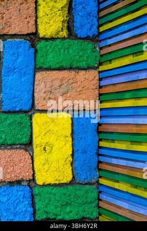 Colorful brick wall with a yellow brick in the middle. The wall is made of different colored bricks, including blue, green, and yellow Stock Photo