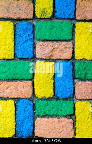 Colorful brick wall with a yellow brick in the middle. The wall is made of different colored bricks, including blue, green, and yellow Stock Photo
