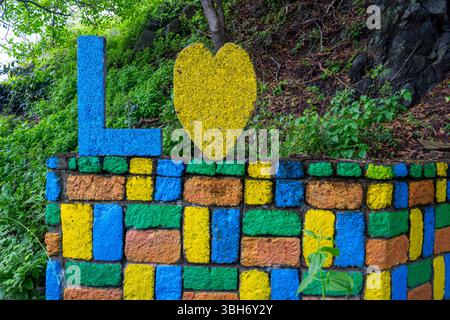 Colorful brick wall with a yellow brick in the middle. The wall is made of different colored bricks, including blue, green, and yellow Stock Photo
