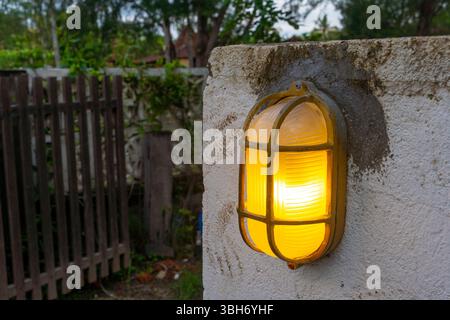Yellow lighted lamp is on a wall. The light is on and the lamp is lit Stock Photo