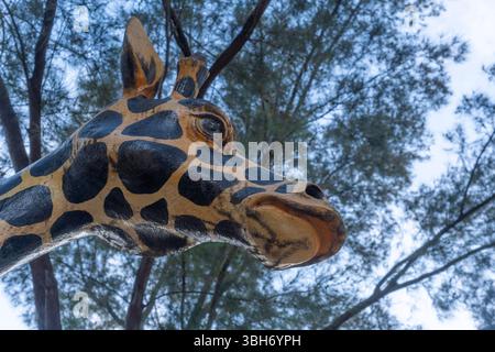 Giraffe statue is sitting on a tree branch. The giraffe has a black and brown pattern on its face Stock Photo