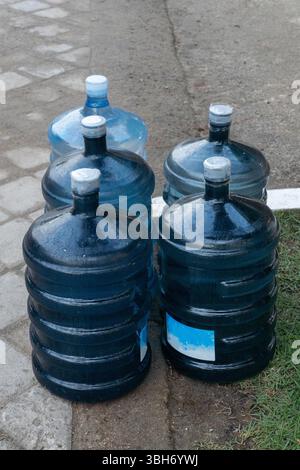 Four large blue water bottles are lined up on a sidewalk. The bottles are all the same size and shape, and they are all filled with water. The bottles Stock Photo