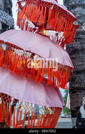 Three pink umbrellas with orange fringes are stacked on top of each other. The umbrellas are decorated with beads and have a warm, inviting feel Stock Photo