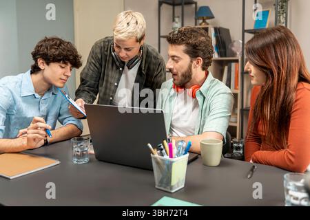 Young multicultural coworkers brainstorming around a laptop in a bright modern office, sharing ideas and planning a creative project together. Stock Photo