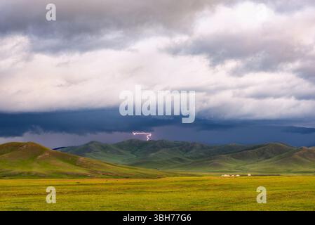 A lightning bolt cuts through stormy skies over Mongolia’s rolling hills, capturing nature’s power and dramatic beauty during a passing thunderstorm Stock Photo