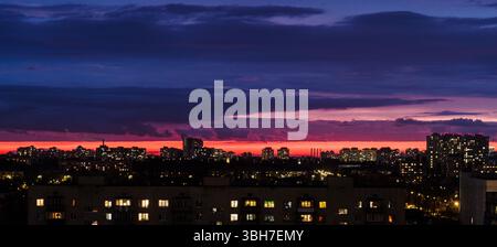 Beautiful sunset in the city. View from the window to the evening city. Fiery sunset in a big city. There are many residential buildings. Stock Photo