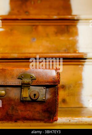 A close-up, slightly high-angle view of an antique, worn leather suitcase. The suitcase is positioned on a wooden surface, possibly a staircase Stock Photo