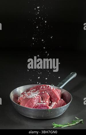 Fresh veal meat with salt on black background. Stock Photo
