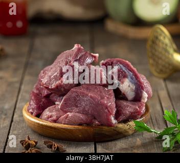 Raw veal chunks in wooden bowl on wooden surface. Stock Photo