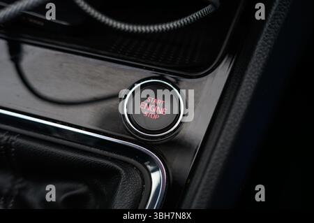 A red start engine button is shown in a black car dashboard. The button is small and red, and it is located in the center of the dashboard. The dashbo Stock Photo