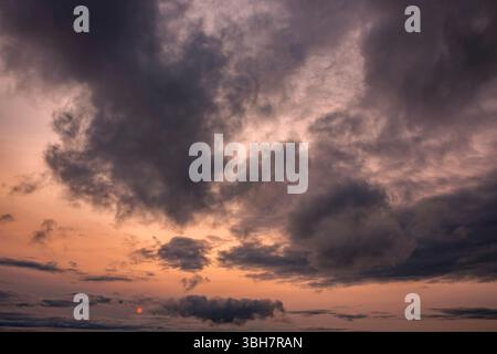 Cloudy sunset background backdrop with the orange sun breaking through the clouds. Stock Photo