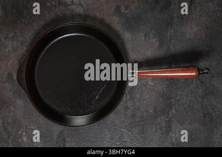 Large cast iron frying pan with wooden handle, well-oiled and empty, top-down view on dark slate surface Stock Photo