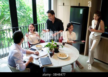An adult Asian business team collaborates, brainstorms ideas during a meeting. They share insights in a modern office, fostering teamwork, achieving s Stock Photo