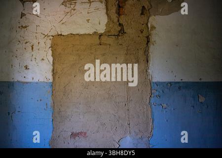 Peeling blue and beige plaster on a damaged wall. Cracks, old paint, and rough texture create an urban decay background for renovation, design, or gru Stock Photo