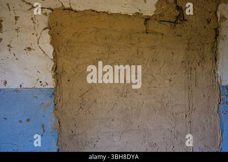 Peeling blue and beige plaster on a damaged wall. Cracks, old paint, and rough texture create an urban decay background for renovation, design, or gru Stock Photo