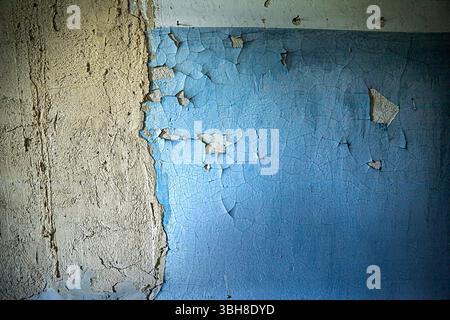 Peeling blue and beige plaster on a damaged wall. Cracks, old paint, and rough texture create an urban decay background for renovation, design, or gru Stock Photo