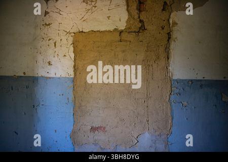 Peeling blue and beige plaster on a damaged wall. Cracks, old paint, and rough texture create an urban decay background for renovation, design, or gru Stock Photo