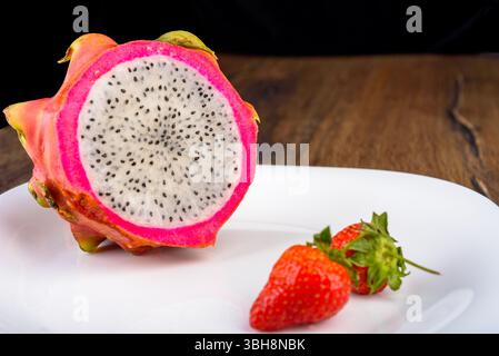 Half a pitahaya or dragon fruit on a plate with strawberries. Copy space. Stock Photo
