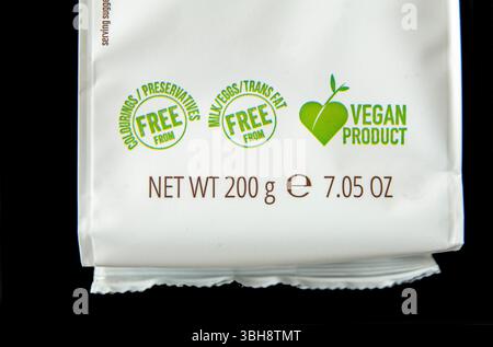 Detail of food package with labels saying vegan product free from colourings, preservatives, milk, eggs and trans fat. Close up image isolated on blac Stock Photo