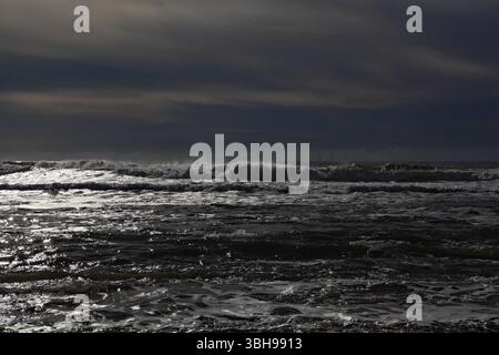 Viana do Castelo, Portugal - February 26, 2025: Powerful ocean waves crash under a dramatic sky with distant offshore wind turbines on the horizon Stock Photo
