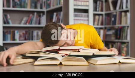 Tired guy napping on books in library Stock Photo