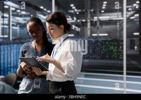 Engineers in data center using device, verifying firewall configurations. Teamworking IT professionals performing equipment vulnerability scans in server hub using tablet Stock Photo