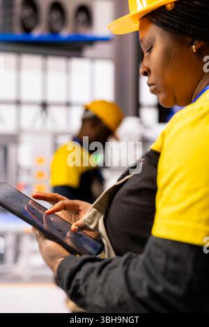 Closeup of engineer utilizing tablet to program and streamline industrial automation, ensuring production efficiency in industry 4.0 facility. Female technician developing automated machinery. Stock Photo