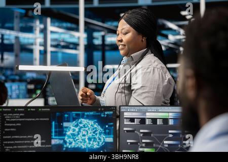 Smiling server room developer using artificial intelligence to enhance operational efficiency and reduce downtime. Happy employee designs and implements AI driven solutions for data center equipment Stock Photo