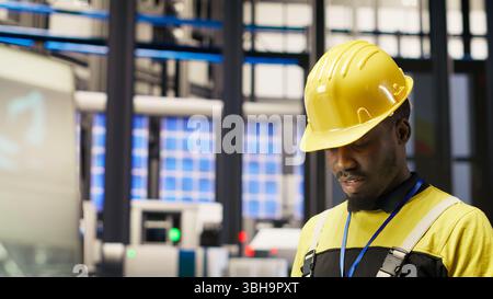 Technician in industrial plant using tablet app to diagnose equipment errors. Manufacturing factory specialist using digital device to coordinate repair tasks on assembly lines, camera B Stock Photo