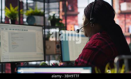 IT support specialist at PC in office helping customers during call, troubleshooting errors. Tech support agent at desk looking at computer monitor, fixing technical issues for clients, camera A Stock Photo