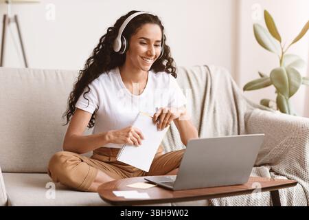 Cheerful lady attending online course, using laptop and wireless headset Stock Photo