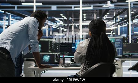 Data center manager supervising worker deploying AI solutions optimizing equipment. Server farm supervisor overseeing programmer using artificial intelligence to minimize systems downtime, camera A Stock Photo