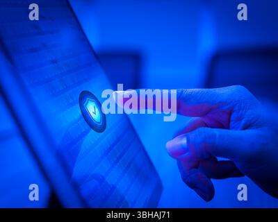 Blue safety shield icon on cyber network background on computer screen while finger scanning for access with biometrics identification. Cyber security Stock Photo