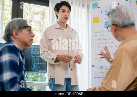 senior programmer bootcamlp,Asian young instructor guides senior learners through a programming on whiteboard, highlighting algorithm thinking and sim Stock Photo