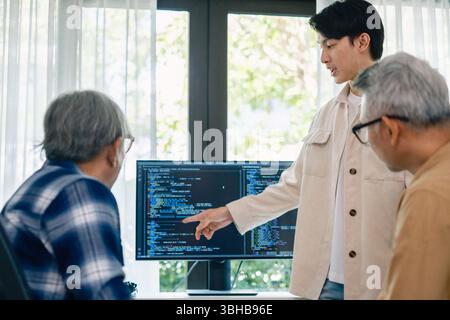senior programmer bootcamlp,Asian young instructor guides senior learners through a programming on whiteboard, highlighting algorithm thinking and sim Stock Photo